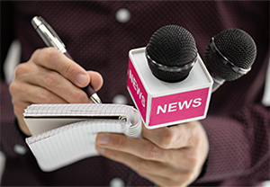 Close up photo of hands holding a news microphone and small tablet and pen.